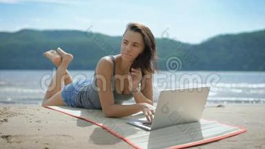 一位年轻漂亮、体贴的<strong>女士</strong>正在沙滩上<strong>用笔记本电脑</strong>躺着汤米